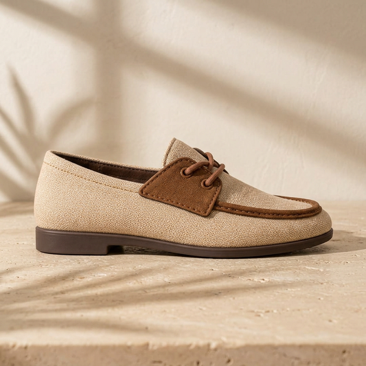 Sand beige boat shoe with brown trim styled on a warm stone surface